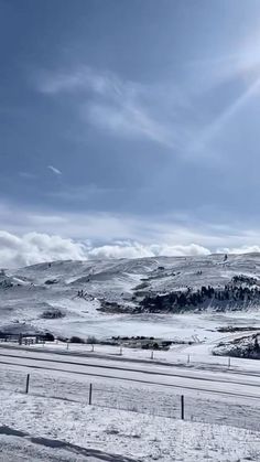 the sun shines brightly on snow covered hills and valleys in the distance, as seen from an empty road