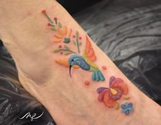 a colorful bird and flower tattoo on the foot