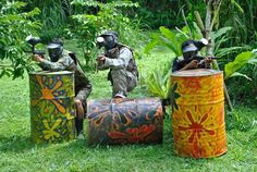 three paintball players are playing with barrels in the grass near some trees and bushes