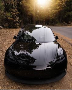 a black sports car parked on the side of a road in front of some trees