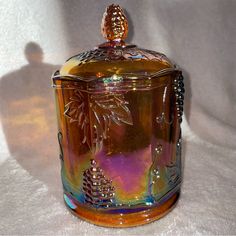 a colorful glass jar sitting on top of a white cloth covered table next to a shadow