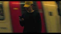 a man wearing a yellow hat is looking at his cell phone while standing in front of a train