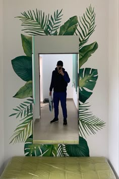 a man taking a selfie in front of a mirror with green leaves on it