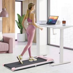 a woman is standing on a treadmill and looking at a laptop computer while wearing pink leggings