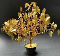 a small tree in a black vase with gold leaves on the top and bottom branches