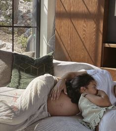 a pregnant woman laying on top of a bed next to a wooden window sill