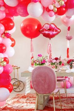 a room filled with lots of pink and red balloons hanging from the ceiling over a dining table