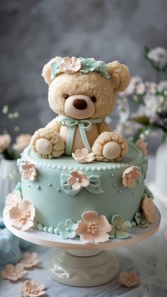 a teddy bear sitting on top of a blue cake covered in frosting and flowers