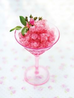 a small glass filled with pink sugar on top of a white table covered in flowers