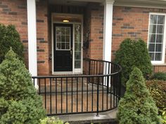 the front door of a brick house with black iron railing and topiary on either side