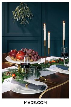 the table is set with candles, plates and fruit on it for an elegant christmas dinner