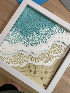 paper cut artwork with footprints in the sand and ocean waves on it's sides