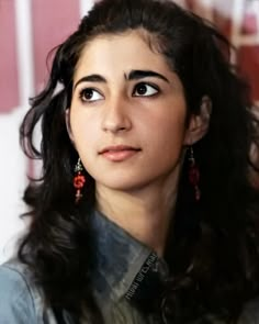 a close up of a person with long hair and wearing red earring's