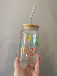 a hand holding a glass with a straw in it and colorful designs on the lid