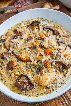 a white bowl filled with mushroom soup on top of a wooden table next to bread