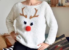 a woman wearing a white sweater with reindeer antlers on it's face and red nose