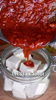 someone is pouring ketchup on cubes of tofu into a glass jar