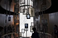 a man standing in front of a tall display with pictures on the wall and people looking at it