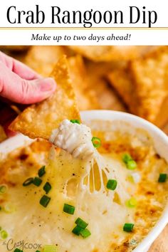 a hand holding a cracker over a bowl of crab rangon dip with green onions