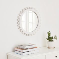 a white dresser with books and a round mirror