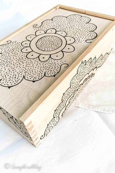 a wooden box sitting on top of a white sheet covered ground with an intricately designed design