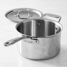 two stainless steel pots with lids and spoons on a white countertop, one is empty