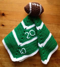 a crocheted green and white scarf with a football on it sitting on a wooden surface