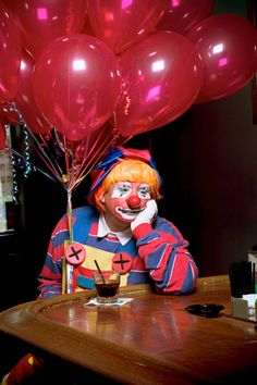 a clown sitting at a table with some balloons