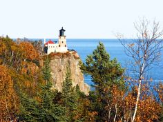 a light house sitting on top of a cliff next to the ocean with trees around it