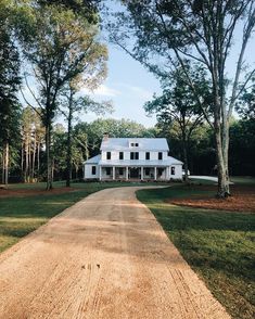 a large white house sitting on top of a lush green field next to tall trees