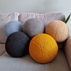 four different colored balls sitting on top of a gray couch next to a green plant