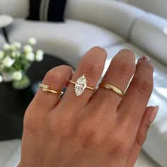 a woman's hand with two gold rings on it and a white couch in the background