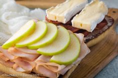 an open faced sandwich with apples and cheese on it sitting on a cutting board next to some bread