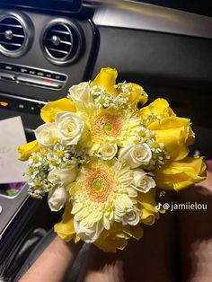 a bouquet of yellow and white flowers in someone's hand next to a car dashboard