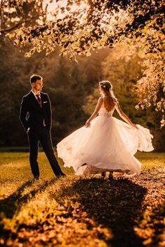 the bride and groom are walking through the park together in their wedding dress, with leaves on the ground