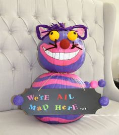 a purple and pink striped ballon with a sign that says we're all mad here