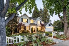 a large white house surrounded by trees and flowers in front of a tree lined driveway