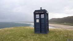 a blue phone booth sitting on top of a grass covered hill next to the ocean