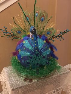 there is a blue and green hat with feathers on it's head, sitting on a lace doily