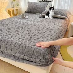 a cat sitting on top of a bed next to a person's hand and foot