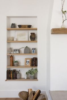 shelves with books and vases on them in the corner of a white walled room