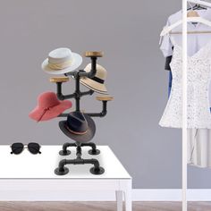 a white table topped with lots of hats next to a dress and hat rack on top of a hard wood floor