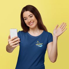 a woman is holding her cell phone and smiling at the camera while wearing a blue t - shirt