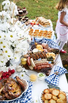 a table filled with lots of food on top of a grass covered field next to white flowers