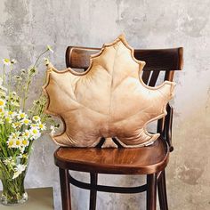 a wooden chair sitting next to a vase with flowers in it and a leaf shaped pillow on the back