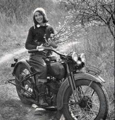 a woman sitting on top of a motorcycle next to a dirt road in the woods