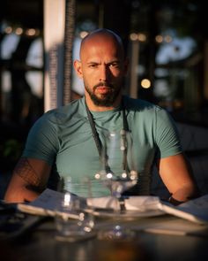 a bald man sitting at a table with wine glasses