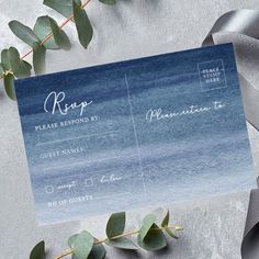 a blue and white wedding card with eucalyptus leaves on it next to a gray ribbon