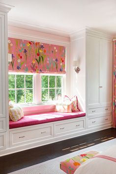 a bedroom with pink and white curtains, window seat, and built - in bookshelves