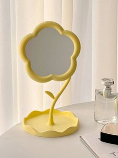 a yellow flower shaped mirror sitting on top of a table next to a glass bottle